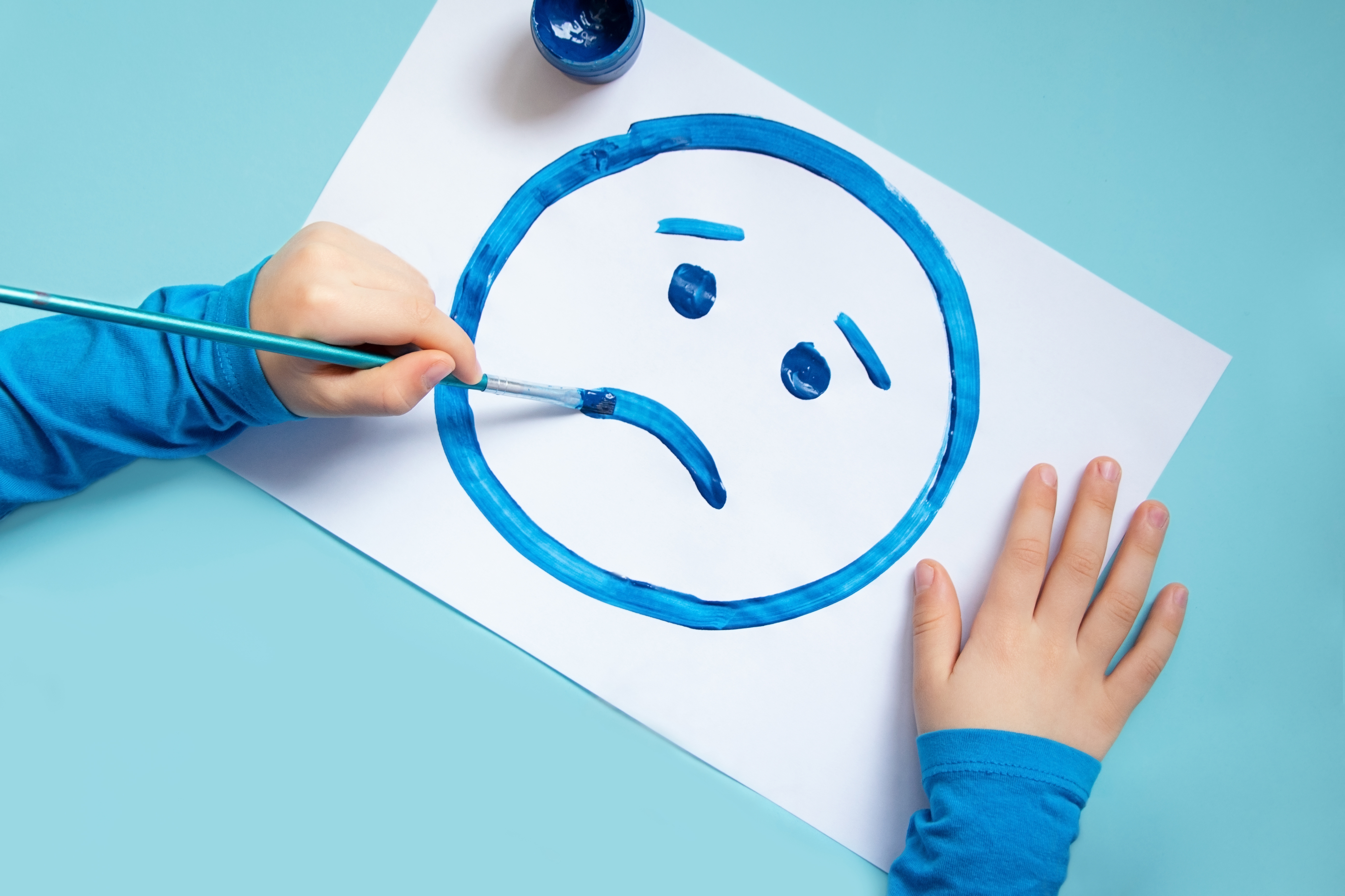 Top view of child drawing sad face. Blue background.